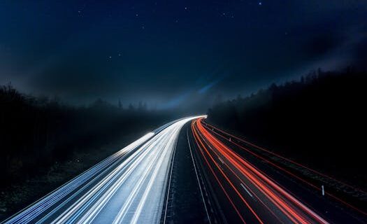 Long exposure night shot capturing stunning red and white light trails on a highway under a starry sky.