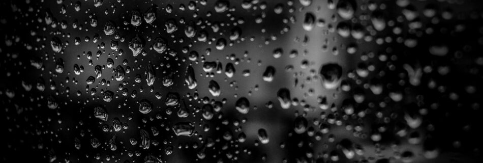 Close-up of raindrops on a glass surface with a dark background, creating an abstract and moody effect.