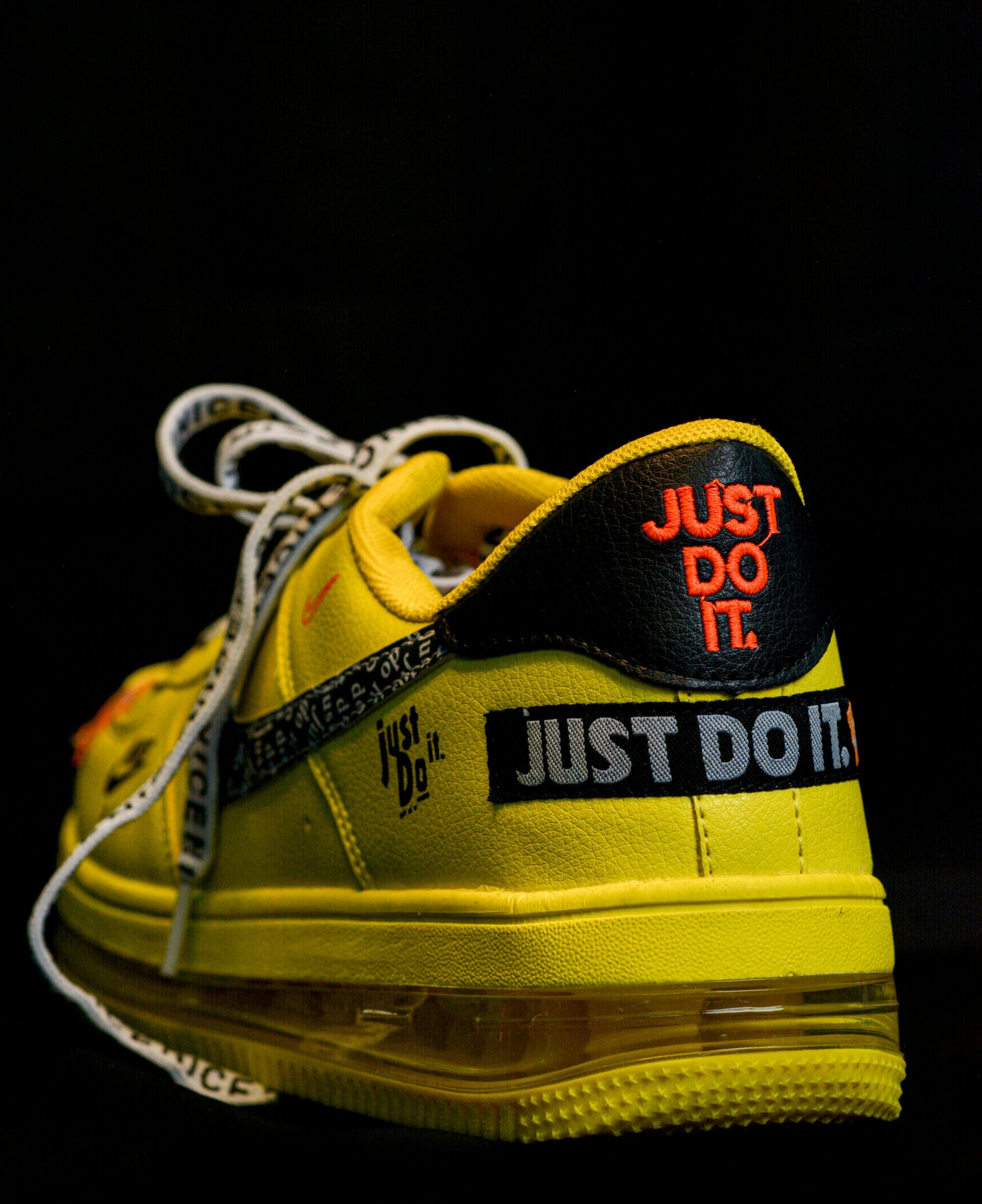 Close-up of a vibrant yellow sneaker featuring a bold slogan, highlighting modern footwear design against a black background.