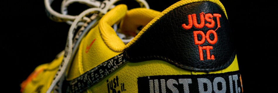 Close-up of a vibrant yellow sneaker featuring a bold slogan, highlighting modern footwear design against a black background.