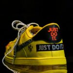 No pain, no gain? Close-up of a vibrant yellow sneaker featuring a bold slogan, highlighting modern footwear design against a black background.